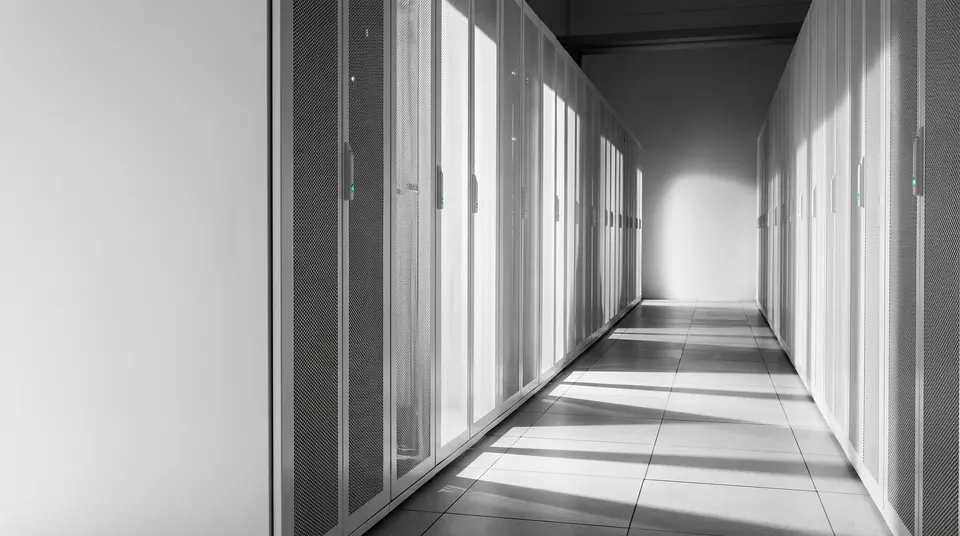 A long, sunlit aisle between rows of white server cabinets with perforated doors